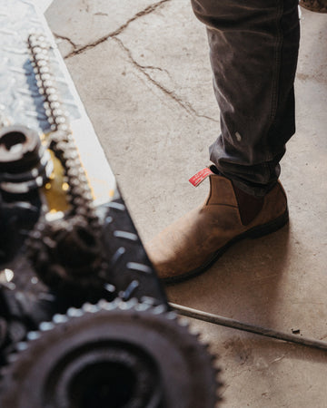 Person wearing brown shoes with a red tag on a concrete floor.