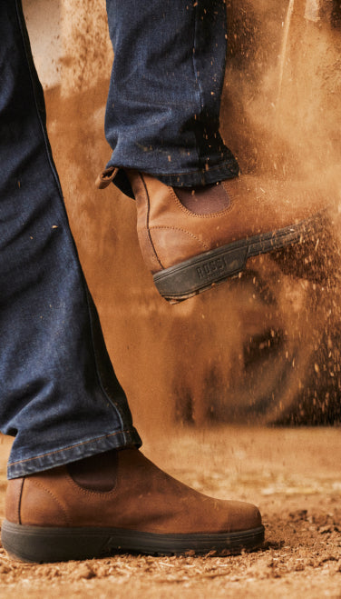 Brown boots stepping into a puddle of water on a sandy background