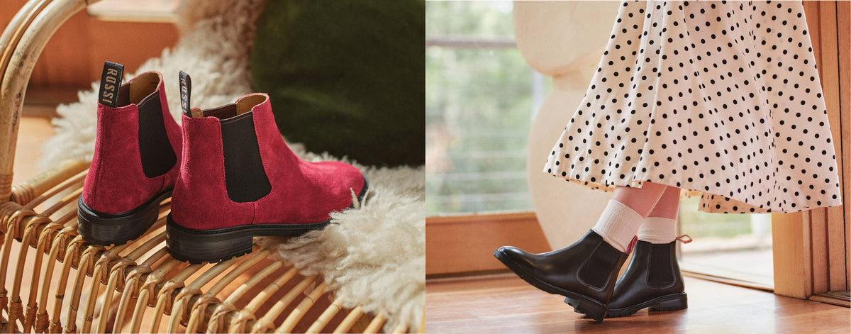 A split lifestyle image showing a pair of burgundy suede Chelsea boots with black elastic side panels on a wicker chair, and a person wearing black Chelsea boots with white socks and a black-and-white polka dot skirt.