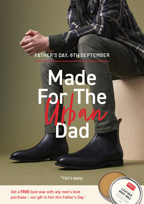 A promotional Father's Day advertisement featuring a man seated on a stool, wearing dark leather Chelsea boots, gray trousers, and a plaid shirt. Large overlaid text reads 'Made For The Urban Dad' with a small inset showing a T&C's Leather Boot Wax tin.